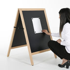 Woman crouching beside a wooden framed blackboard A-frame, attaching a poster to the chalkboard panel