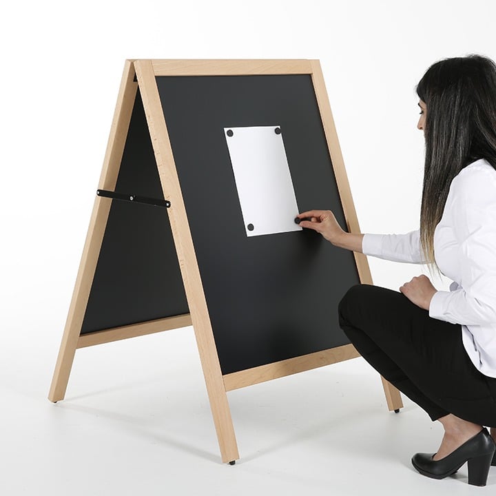 Woman crouching beside a wooden framed blackboard A-frame, attaching a poster to the chalkboard panel