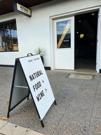Black A-frame on a footpath outside a restaurant reading Natural Food and Wine with an arrow