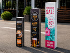 Three printed bollard signs in a car park advertising a coffee special, happy hour and a mid season sale