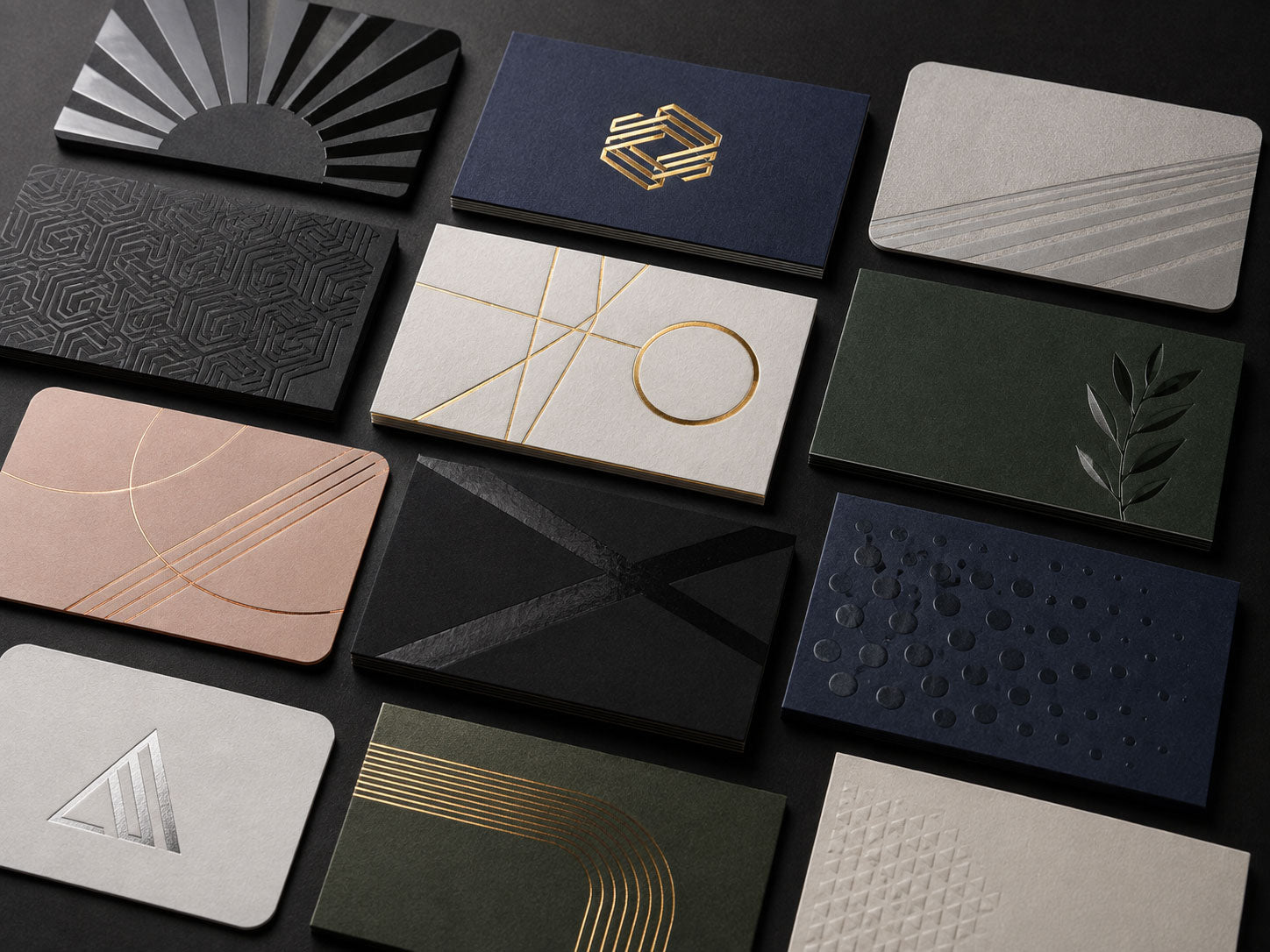 Twelve luxury business cards on a black surface in gold foil, embossed and textured finishes