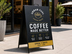 Black metal faced A-frame sign on a footpath outside a coffee house, printed with gold and white artwork
