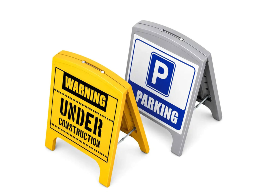 Two moulded plastic A-frame signs, one yellow reading Warning Under Construction and one grey showing a blue parking symbol