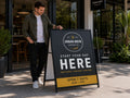 Man standing beside a black A-frame sign outside a coffee shop, the printed insert reading Start Your Day Here
