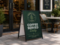 Black A-frame sign on a footpath outside a cafe with a dark green printed corflute insert