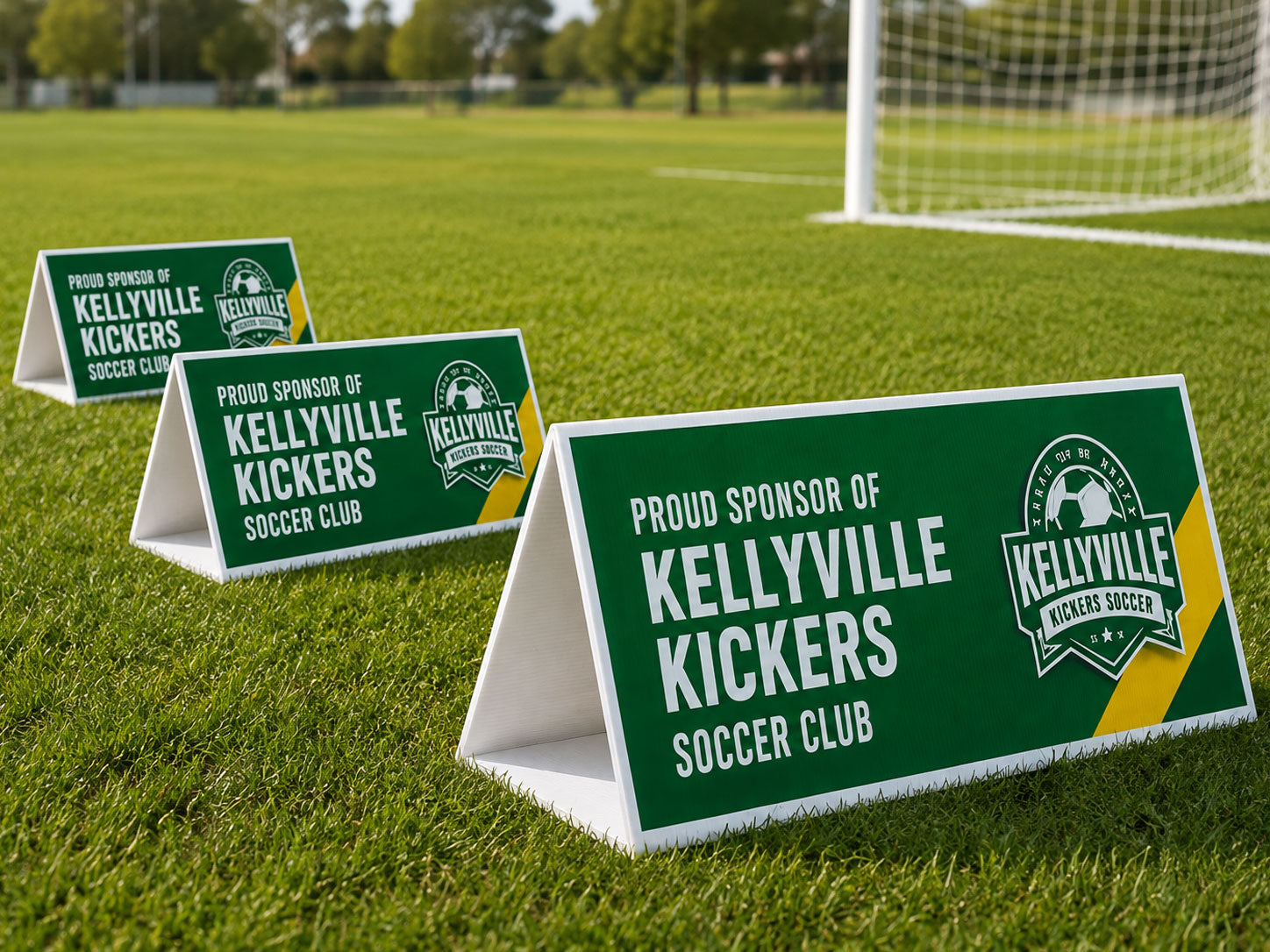 Three green triangle roster signs standing on the grass beside a soccer goal, printed for a club sponsor