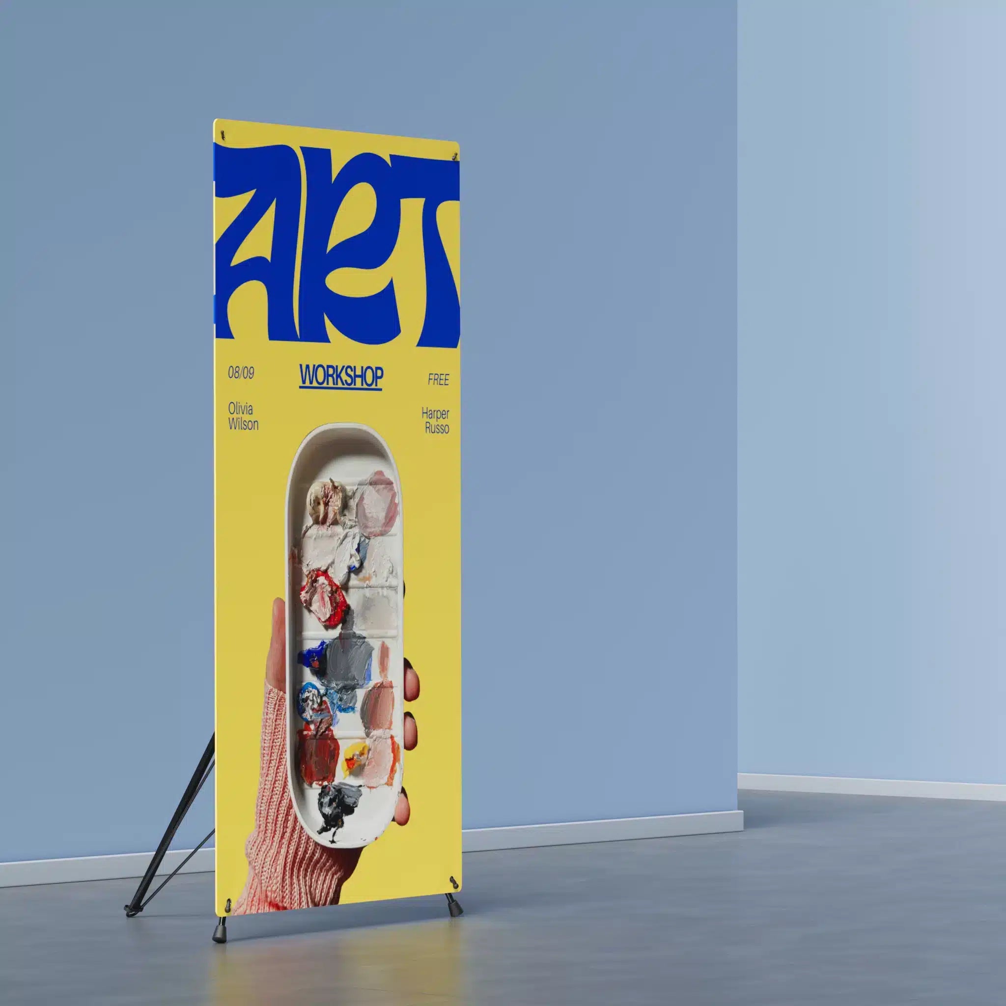 X frame banner stand displaying an art workshop print in a room with blue walls