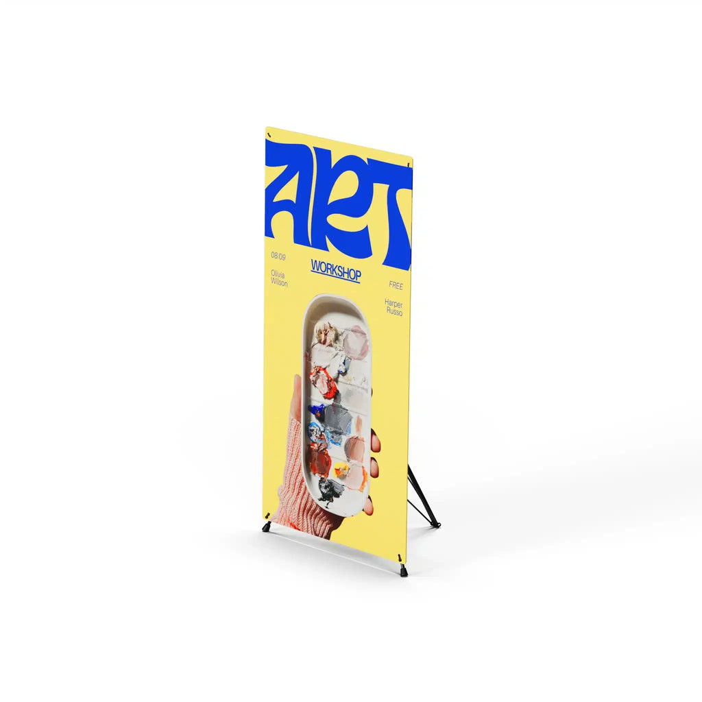 X frame tripod stand holding a yellow and blue art workshop banner, viewed from an angle