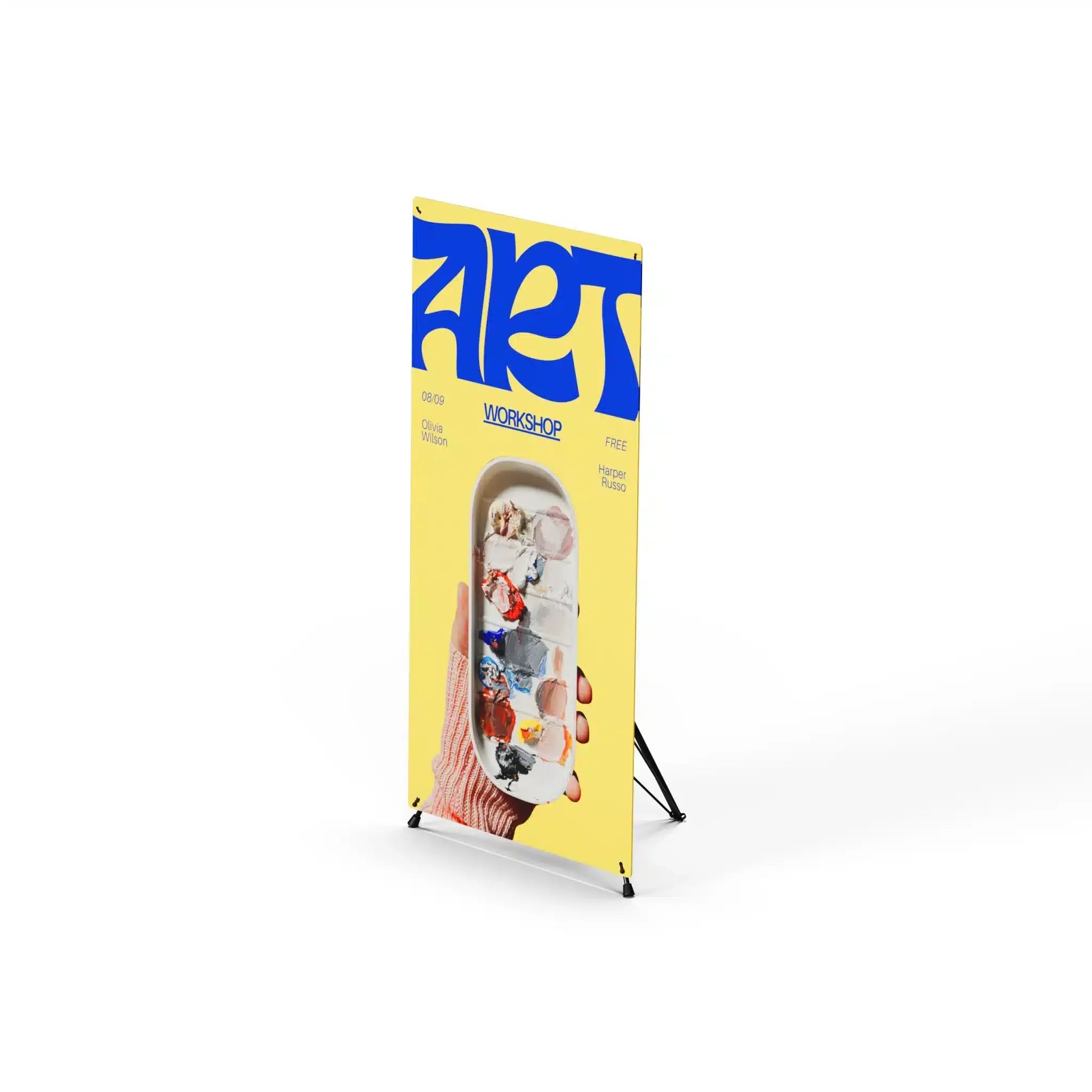 X frame tripod stand holding a yellow and blue art workshop banner, viewed from an angle